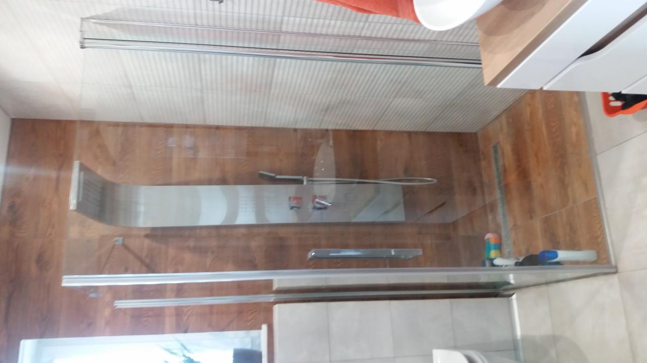 Kabina prysznicowa z panelem natryskowym i drewnopodobnymi płytkami na ścianach, widok z góry, z elementami wyposażenia łazienki.