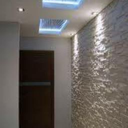 Igbud - Nowoczesne wnętrze: ściana z dekoracyjną fakturą kamienia, podświetlane panele sufitowe z motywem fal, minimalistyczne oświetlenie punktowe i ciemne drzwi.