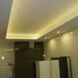 Nowoczesna łazienka z podwieszanym sufitem i oświetleniem punktowym LED, jasne płytki na ścianach, ciemna zabudowa.