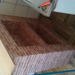 Niski, podwójny regał z obudową z płyty meblowej i wykończeniem imitującym cegłę, ustawiony na drewnianej podłodze w jodełkę, widok z góry pod kątem.