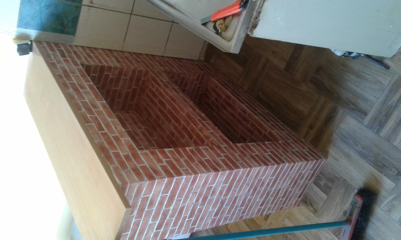 Niski, podwójny regał z obudową z płyty meblowej i wykończeniem imitującym cegłę, ustawiony na drewnianej podłodze w jodełkę, widok z góry pod kątem.