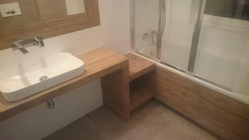 Nowoczesna łazienka z umywalką nablatową na drewnianym blacie, obok wanna z zabudową z drewna, szklany parawan nawannowy, płytki imitujące drewno na ścianach i podłodze.