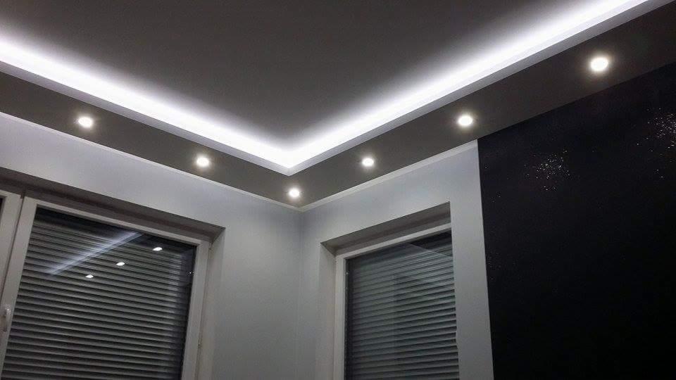 Nowoczesne wnętrze z podwieszanym sufitem z oświetleniem LED i punktowymi lampami, ściany w odcieniach szarości i czerni, okna z żaluzjami.