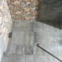 FHU LIDER Jerzy Hućko - Wykończona łazienka z szarymi płytkami imitującymi drewno na podłodze i ścianach, oraz dekoracyjną ścianą z motywem plastrów drewna.