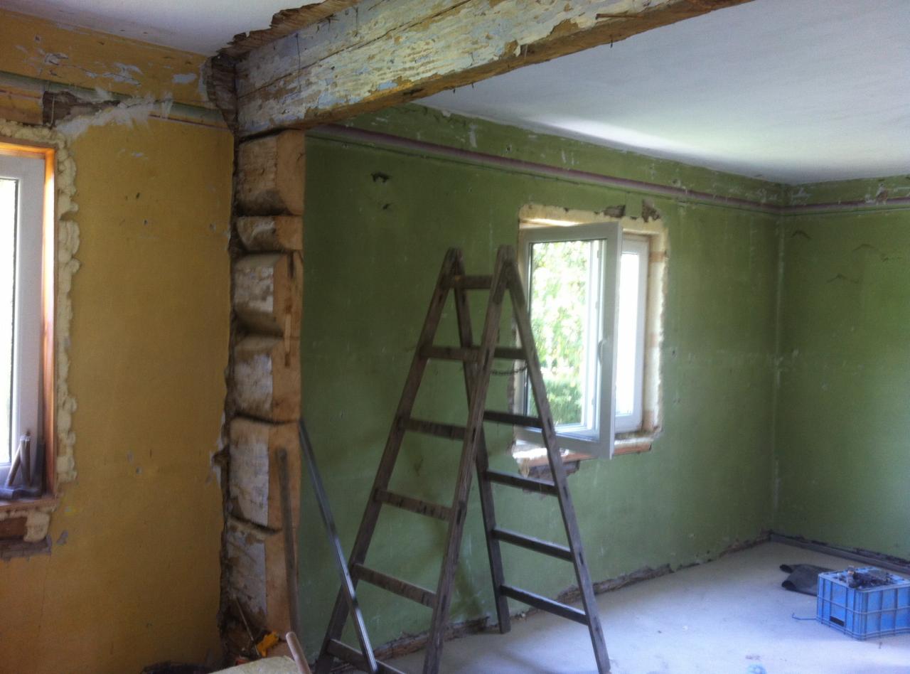Pokój w trakcie remontu: zielone ściany, drewniana drabina, odsłonięta drewniana belka stropowa z resztkami farby, okno w trakcie osadzania, żółta ściana z pianką montażową wokół okna.