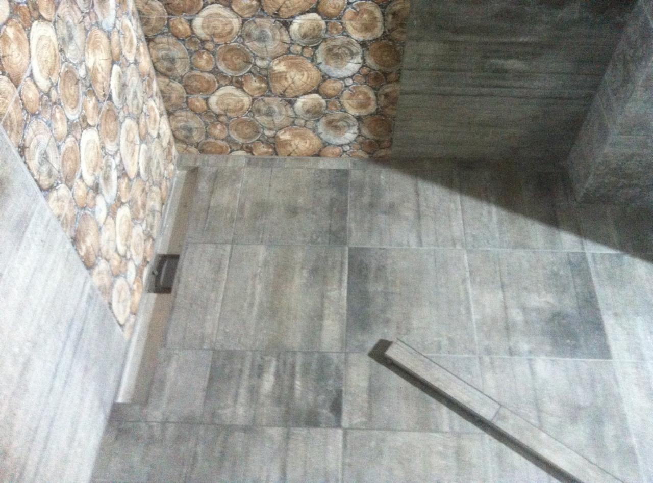 Wykończona łazienka z szarymi płytkami imitującymi drewno na podłodze i ścianach, oraz dekoracyjną ścianą z motywem plastrów drewna.