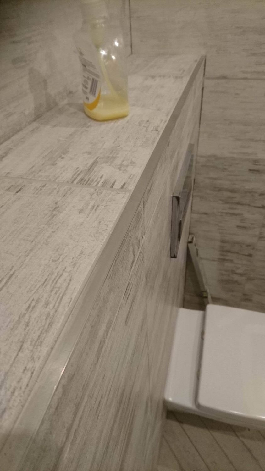 Ukończona zabudowa umywalki z płytek imitujących drewno, z widocznym syfonem i butelką z płynem do mycia rąk, sfotografowana pod kątem z bliska.