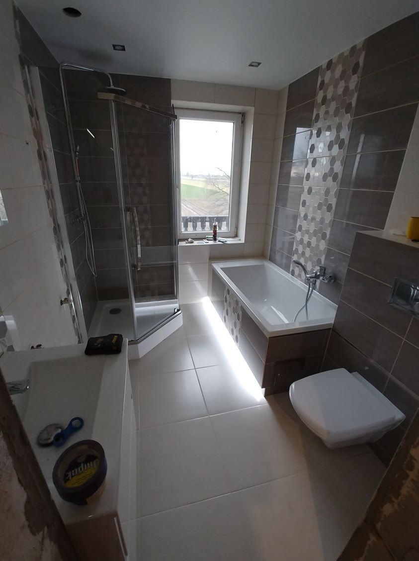 Wykończona łazienka z kabiną prysznicową, wanną z podświetleniem LED, toaletą i umywalką. Na umywalce widoczne narzędzia i materiały budowlane.