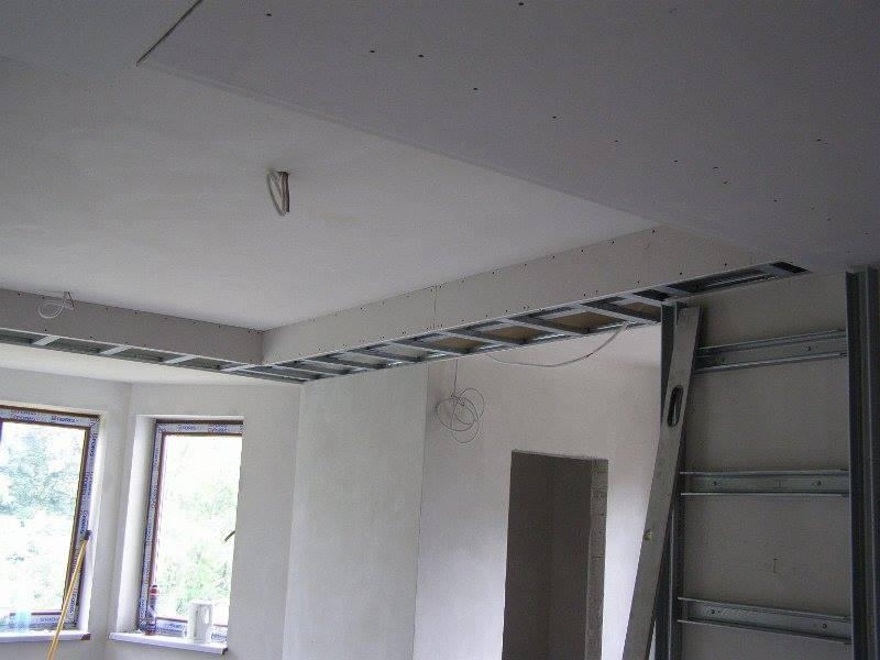 Montaż sufitu podwieszanego z płyt kartonowo-gipsowych na metalowej konstrukcji, widoczna poziomica i wystające kable elektryczne.