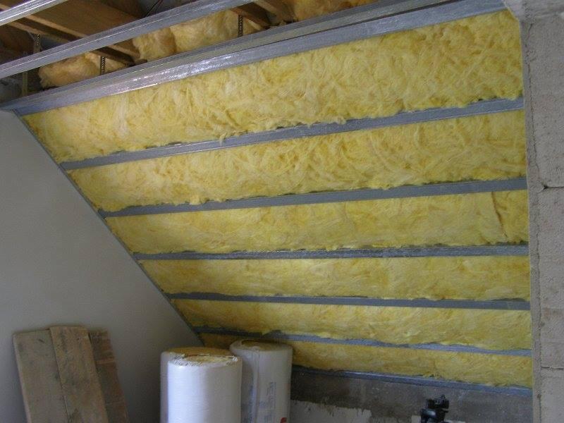 Izolacja poddasza wełną mineralną w Olsztynie, widoczne metalowe profile konstrukcyjne i rolki materiału izolacyjnego.