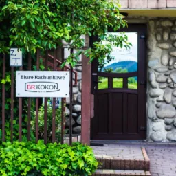 Wejście do biura rachunkowego BR Kokon z widoczną tablicą informacyjną, zielenią i elementami kamiennej elewacji.