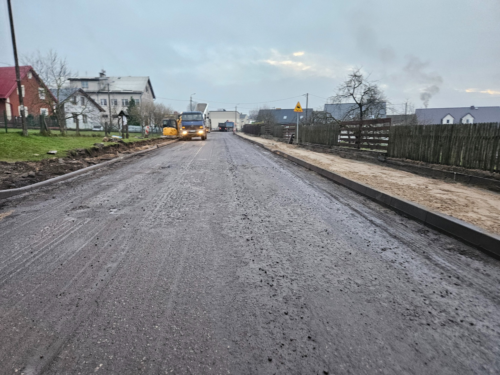 Przygotowanie podłoża pod chodnik i drogę w terenie zabudowanym, widoczny ciężki sprzęt i wykopane pobocze.