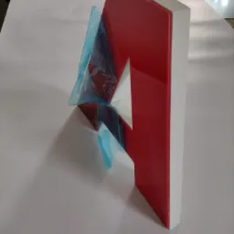 Czerwona, przestrzenna litera z wyciętym białym kształtem gwiazdy, zabezpieczona częściowo niebieską folią ochronną, leżąca na białym podłożu, widoczny jej bok i krawędzie.