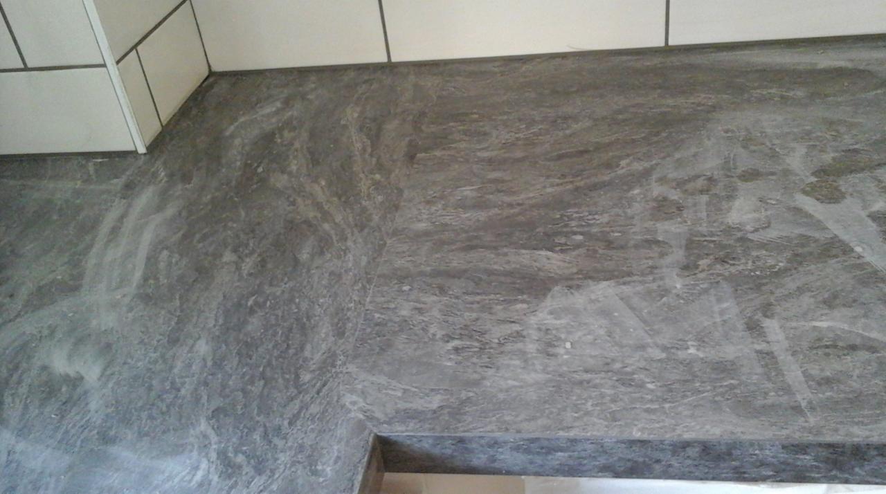 Szara, marmurkowa podłoga w łazience po remoncie, widoczne ślady pyłu budowlanego i fragment białych płytek ściennych.