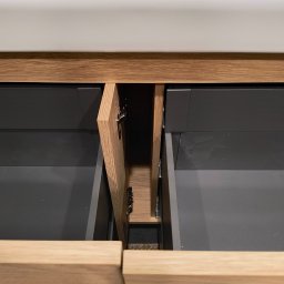 Zabudowa Wnętrz Artur Retke - Otwarta szafka pod umywalką z drewnianymi frontami i szarymi szufladami, widoczne zawiasy.