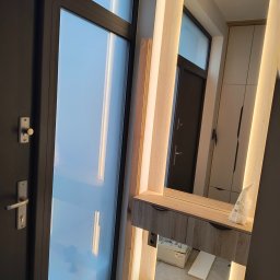 Zabudowa Wnętrz Artur Retke - Zamknięte drzwi balkonowe z widoczną skrzynką narzędziową Festool u dołu, obok toaletka z oświetleniem LED i lustrem, w którym odbija się szafa.