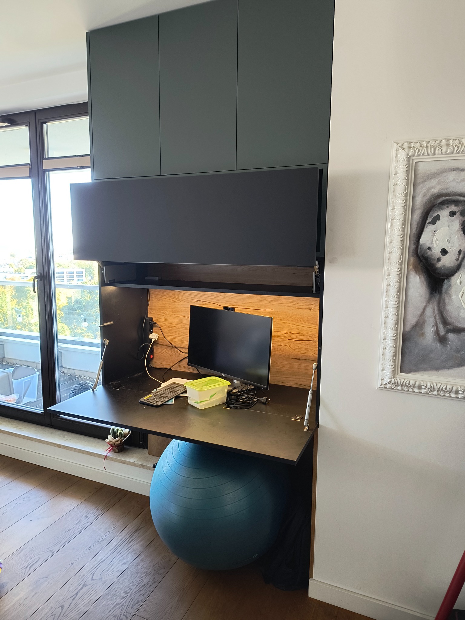 Szafa wnękowa z biurkiem opuszczanym, pod spodem piłka do ćwiczeń, widok na zewnątrz przez okno