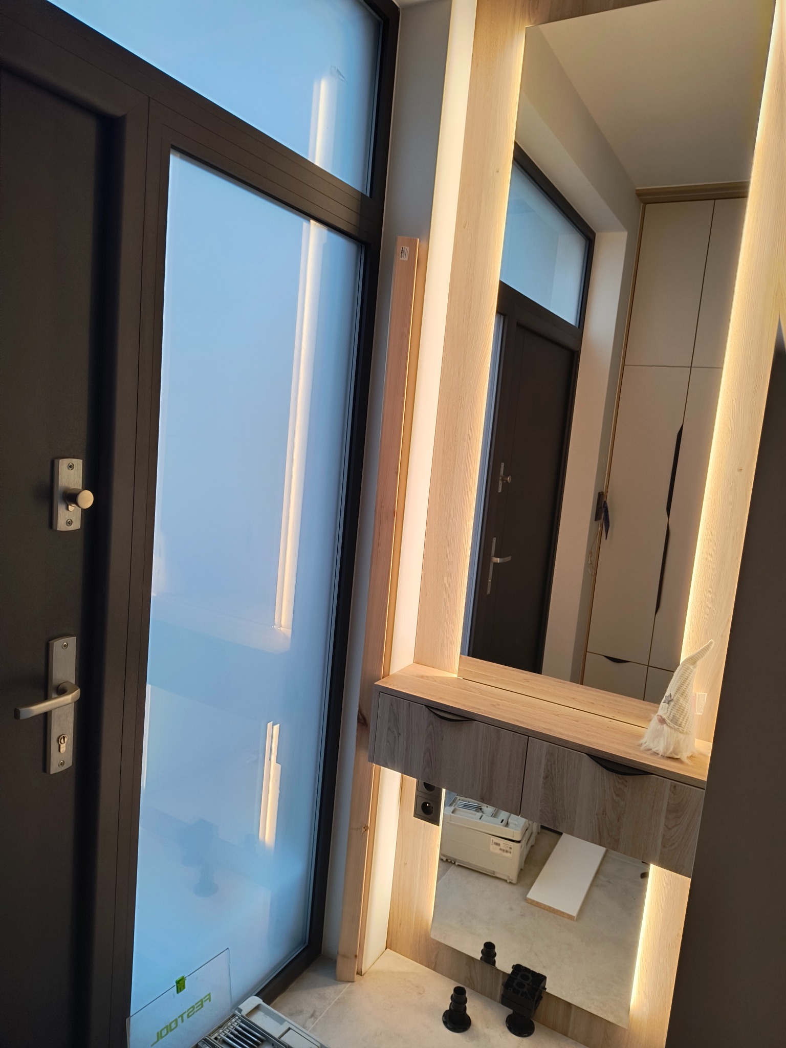 Zamknięte drzwi balkonowe z widoczną skrzynką narzędziową Festool u dołu, obok toaletka z oświetleniem LED i lustrem, w którym odbija się szafa.