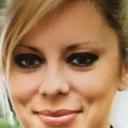 Portret kobiety z blond włosami, ciemnym makijażem oczu i delikatnym uśmiechem, skierowanej wprost.