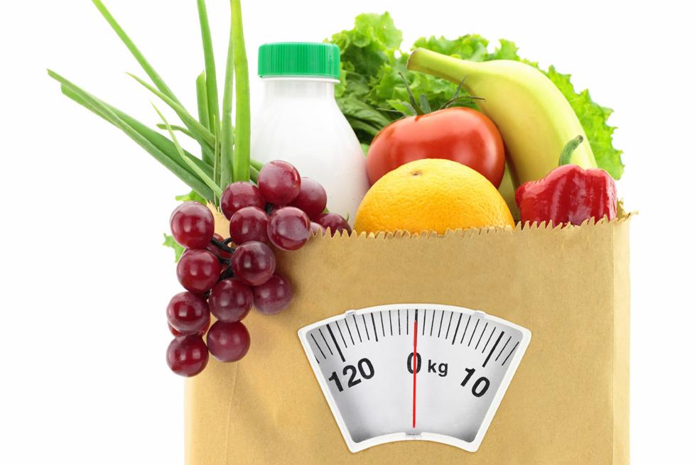 Papierowa torba z owocami, warzywami i butelką mleka, z naklejoną wagą wskazującą zero kilogramów.