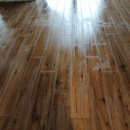 Mir-pol - Świeżo ułożona, błyszcząca podłoga z płytek imitujących drewno, z widocznymi refleksami światła i fugami, w trakcie czyszczenia lub schnięcia.