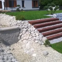 Ogród z elementami skalnymi, drewnianymi schodami i gabionami, świeżo założony trawnik, widok z perspektywy lekko z góry.