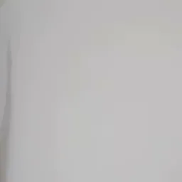 Natryskowe nakładanie białej warstwy na ścianę w trakcie remontu, widoczny fragment ramienia trzymającego pistolet z niebieskim wężem.