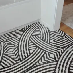 Czarno-biała podłoga z wzorem geometrycznym w łazience, widok z góry, z fragmentem wanny i progiem drzwi.