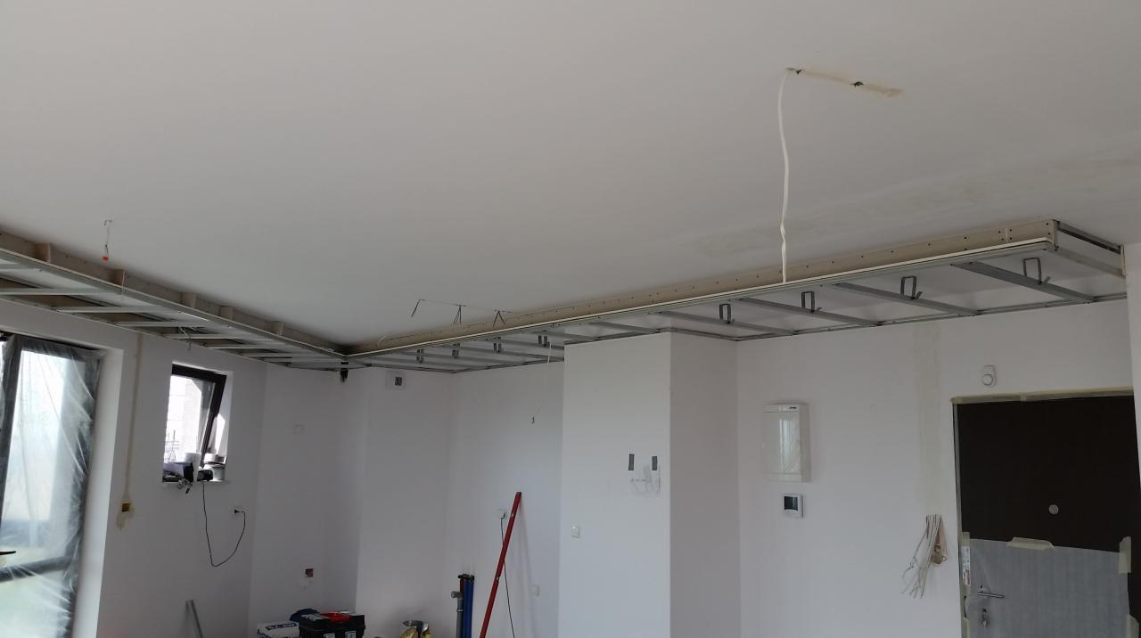 Montaż metalowej konstrukcji sufitu podwieszanego w jasnym pomieszczeniu, widoczne profile i przewody elektryczne.