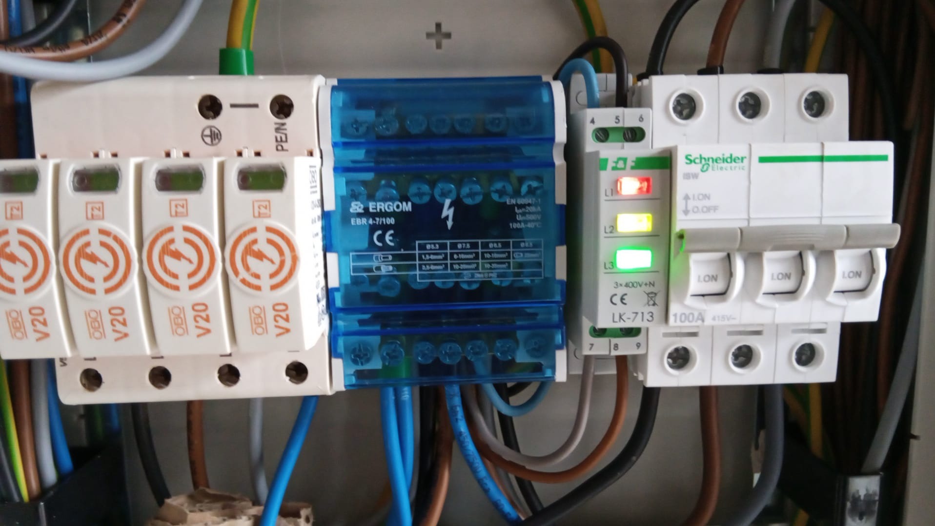 Szczegółowy widok rozdzielnicy elektrycznej z ogranicznikami przepięć OBO V20, modułem ERGOM EBR 4-7/100 i wyłącznikiem Schneider Electric ISW LK-713, widoczne przewody i złącza.