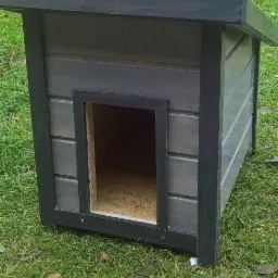 Drewniana buda dla psa z ciemnoszarą impregnacją, ustawiona na trawniku.