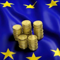 Stosy złotych monet z symbolem na tle flagi Unii Europejskiej, symbolizujące wsparcie finansowe.