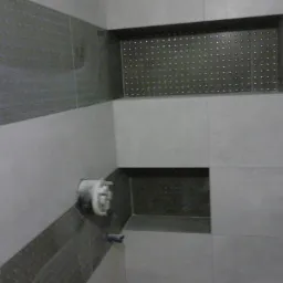 Wykończona ściana w łazience z szaro-białymi płytkami, wnękami z dekoracyjnym tłem i zamontowaną baterią prysznicową.