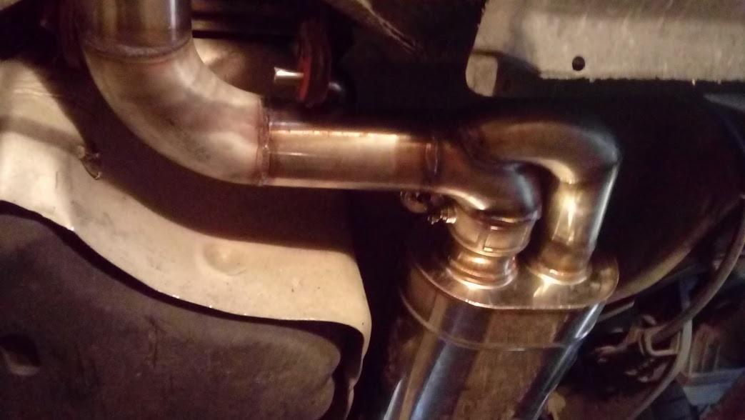 Nowy, błyszczący układ wydechowy z widocznymi spawami, zamontowany pod samochodem, z gumowym mocowaniem tłumika