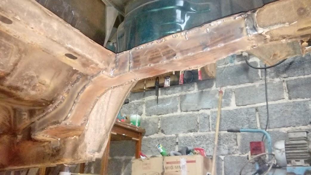 Fragment podwozia samochodu po naprawie blacharskiej i wzmocnieniu elementami, widoczne spawy, tło stanowi ściana z szarych cegieł.