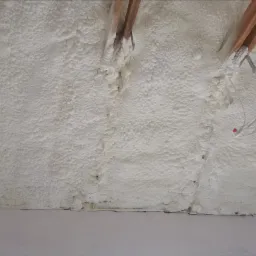 Poddasze ocieplone białą pianką PUR, widoczne drewniane belki stropowe i fragment instalacji elektrycznej.