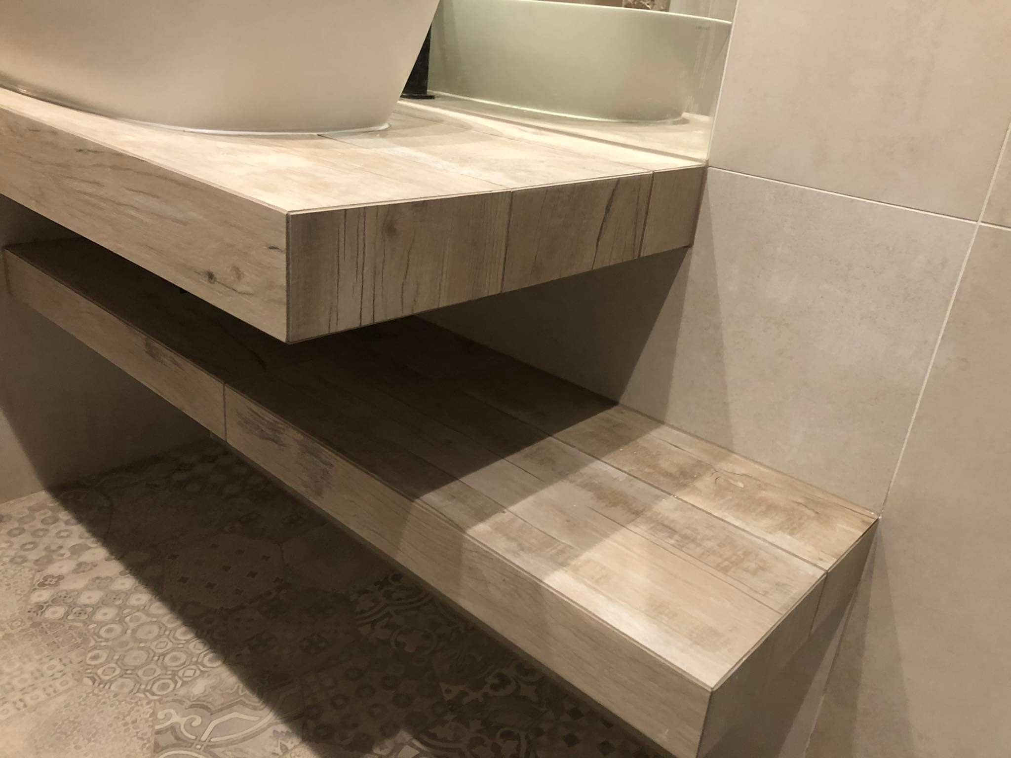 Drewnopodobna półka w łazience, wykonana z płytek. Widoczna umywalka nablatowa, płytki ścienne i podłogowe z wzorem. Ujęcie z bliska, prezentujące detale wykończenia.