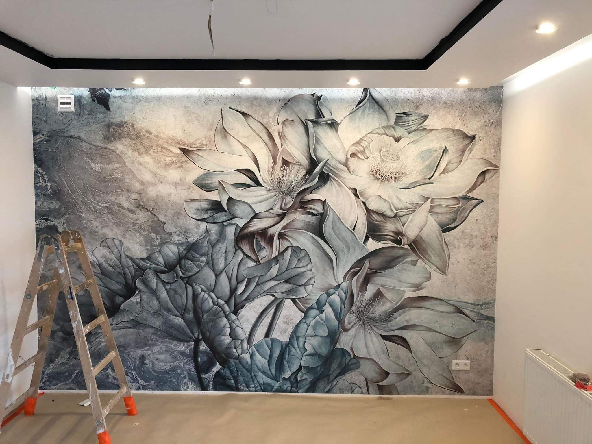 Fototapeta z motywem kwiatowym na ścianie w pokoju, drabina malarska z boku. Wykończone wnętrze z oświetleniem sufitowym i listwami.