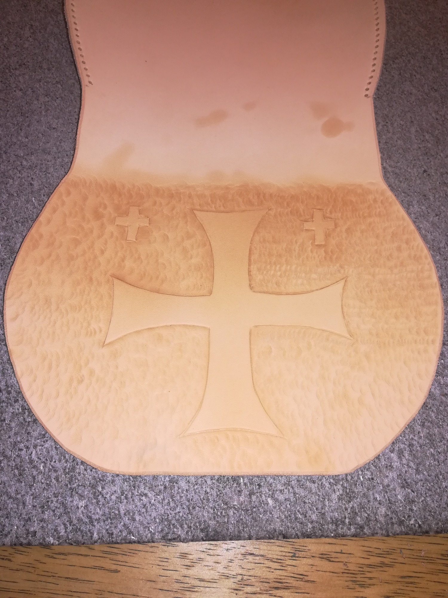 Skórzany element z wytłoczonym krzyżem maltańskim, widoczne ślady obróbki i dziurki na szwie.