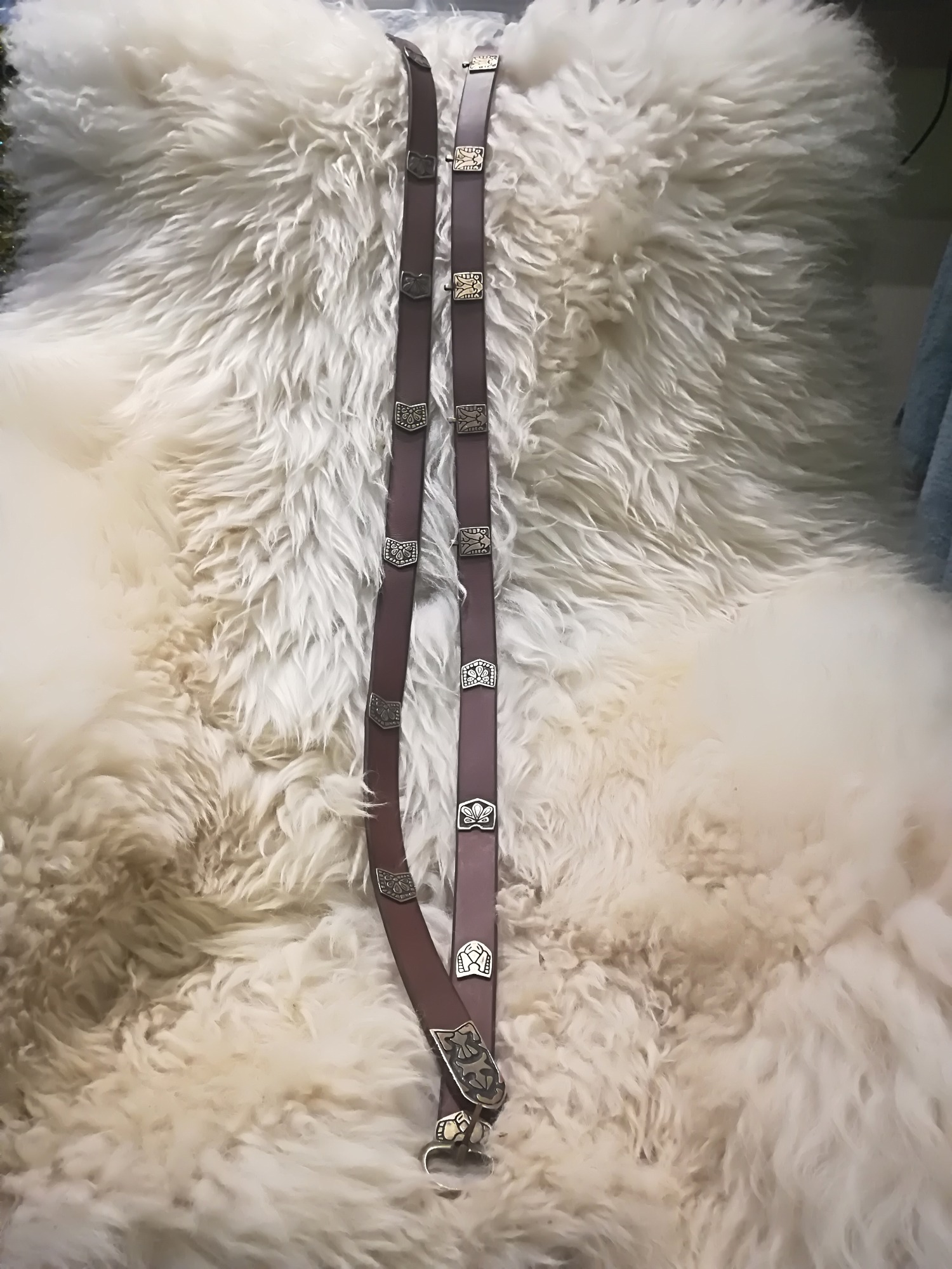 Dwa skórzane pasy z metalowymi zdobieniami leżące na białym, puszystym futrze.