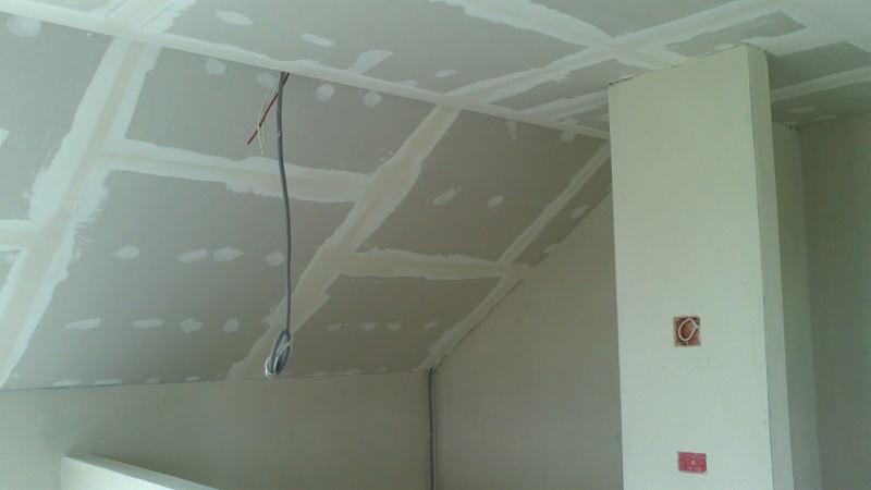 Skośny sufit poddasza z płyt kartonowo-gipsowych, widoczne łączenia płyt zaszpachlowane, wiszący kabel elektryczny, puszki elektryczne w ścianie.