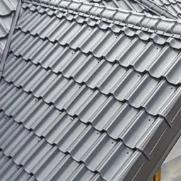 Nowoczesne, grafitowe pokrycie dachowe z blachodachówki modułowej, widoczne z bliska w słoneczny dzień, z fragmentem okna w tle.