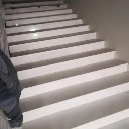 Białe schody kamienne z widocznymi śladami montażu i zabezpieczeniem folią, prowadzące w górę, w trakcie wykańczania.