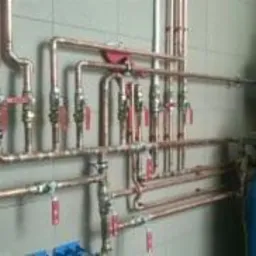 Instalacja centralnego ogrzewania z miedzianych rur z licznymi zaworami i dwoma zbiornikami ciśnieniowymi w szarej kotłowni.