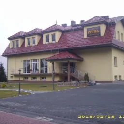 Żółty budynek usługowy z czerwonym dachem i szyldem 'Dom Weselny Petra', widok z zewnątrz w pochmurny dzień.