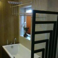 Nowoczesna łazienka z wanną, grzejnikiem drabinkowym w geometrycznym wzorze i suszarką podsufitową, widok z boku.