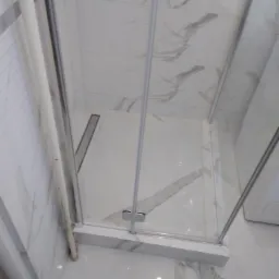 Kabina prysznicowa z białymi płytkami imitującymi marmur, z odpływem liniowym w podłodze.