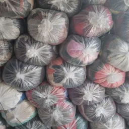 Stos przezroczystych worków foliowych wypełnionych tekstyliami w różnych kolorach i wzorach, ciasno ułożonych jeden na drugim.