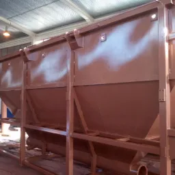 Metalowa konstrukcja z trzema zbiornikami o stożkowym kształcie, świeżo pomalowana brązową farbą proszkową, widoczna w hali produkcyjnej pod sztucznym oświetleniem.