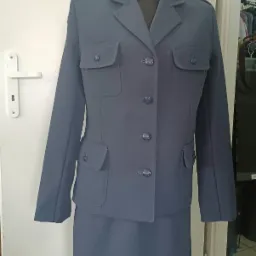 Damski, dwuczęściowy uniform w odcieniu szaro-niebieskim, z widocznymi kieszeniami i guzikami, zaprezentowany na manekinie na tle białych drzwi.